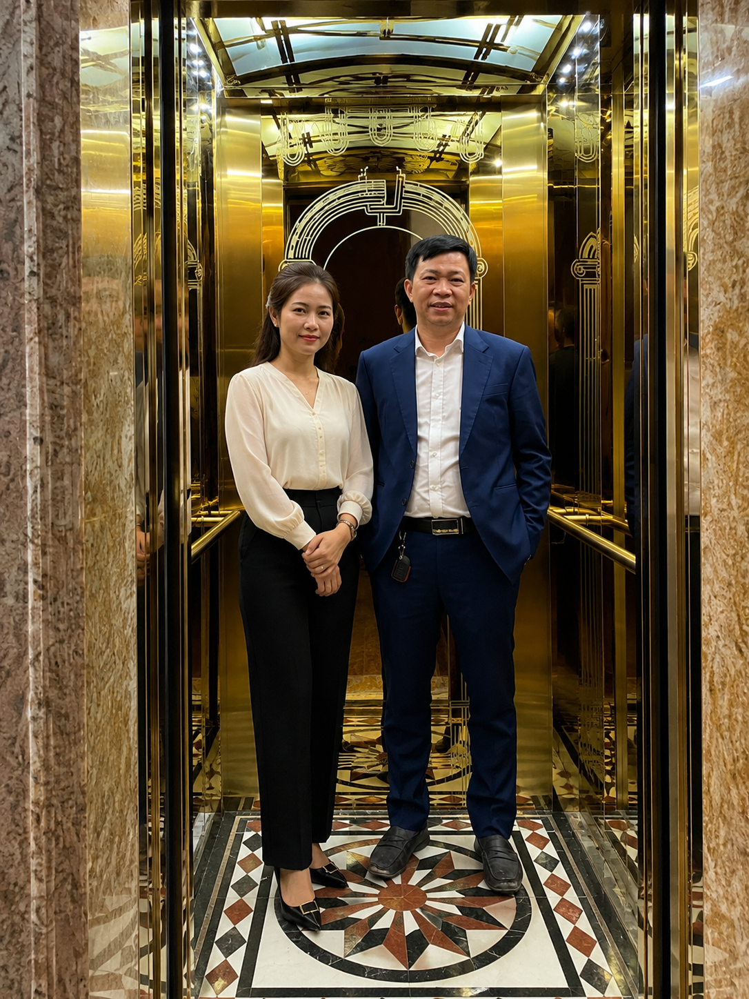 Thang máy nội thất mạ vàng sang trọng với hai người mặc đồ công sở đứng bên trong